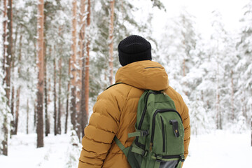 Fototapeta na wymiar man with a backpack on his back walks in a snowy forest. guy enjoys the winter nature in the park.