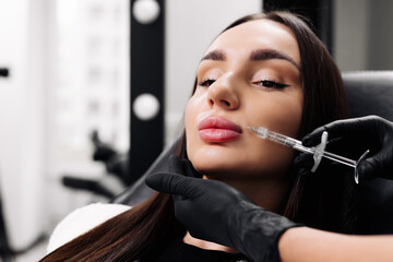 Close-up of a woman's face. A cosmetologist in medical gloves pierces a woman's lip with a syringe...