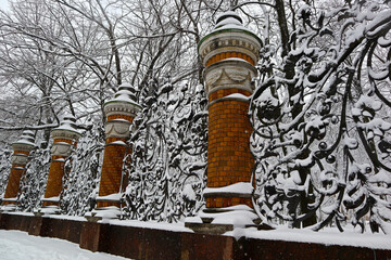 Garden trellis covered with white snow during winter snowfall. Detail of decorative fence of Mikhailovsky Park in St. Petersburg (Russia) on a cloudy snowy day.