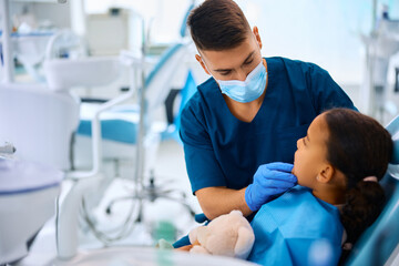 Dentist examining teeth of little black girl at dental clinic.