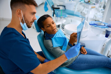 Black woman and her dentist examining dental X-ray during appointment at dental clinic.