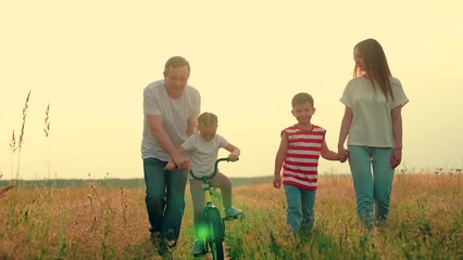 Mom, father, son, daughter, cycling outdoors. Dad teaches child ride bike on path. Girl, boy learns...