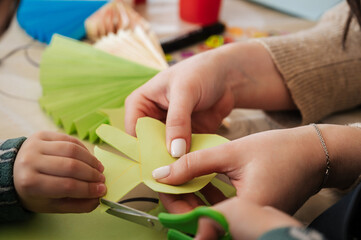 hands make crafts from colored paper at the table
