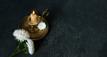 Burning candle in candlestick, white chrysanthemums flowers on dark abstract backdrop. symbol of...