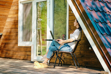 Digital nomad with laptop on veranda of tiny house - obrazy, fototapety, plakaty