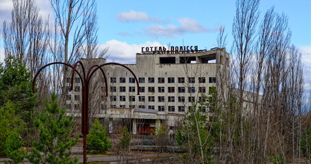 A dilapidated building with broken windows surrounded by overgrown trees.