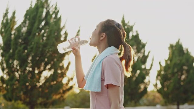 Sport woman is drinking water and cooldown after running in the park.