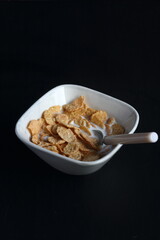Bowl of cereal, cornflakes with milk in a bowl on a black background