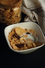 Bowl of cereal, cornflakes with milk in a bowl on a black background