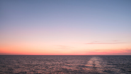 Beautiful red sunset over the blue sea horizon behind the stern of a sailing ferry ship