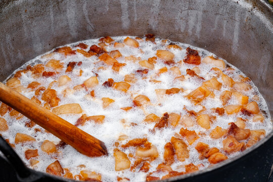 Preparation of delicious unhealthy fried pork greaves in a cauldron on the open fire. Delicious fried pork greaves in the pan traditional Romanian Christmas dish. Crispy deep fried