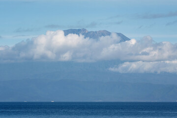 View from Nusa Penida island of Mount Agung covered with clouds on sunny day. Bali, Indonesia.