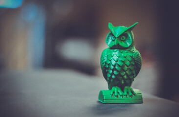 The green form in the form of a small owl created on a 3d printer stands on the surface of a dark...