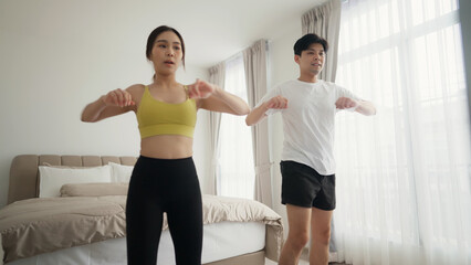 Fototapeta na wymiar Young couple in sportswear are doing exercises together at home on morning. Enjoying cardio activity. 