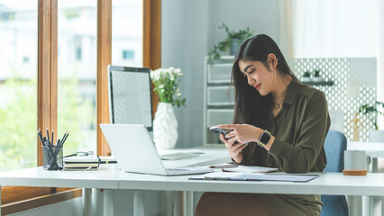 Portrait of young woman designer using smartphone at office. Technology and user interface design concept.