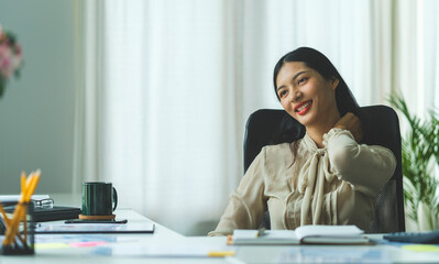 Satisfied asian young woman relaxing at her workplace and looking through the window at office.