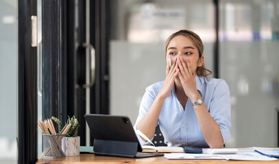 Stressed woman with mouth in hand leaning on table at home office.
