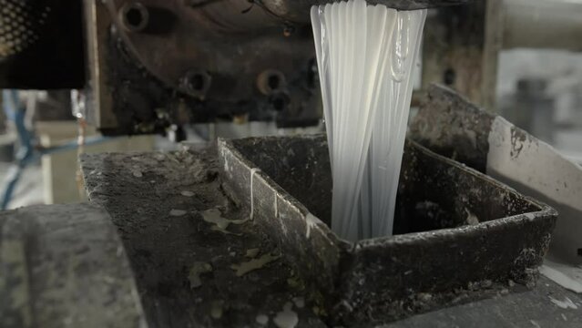 Hot plastic flows pouring into metal container in plant workshop closeup. Waste polyester materials reusing with factory facility