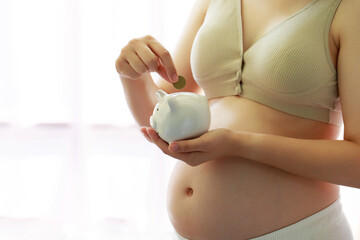 A pregnant woman drop a golden coin into a piggy bank, Saving money for prepare in future and the newborn baby. Money saving, donation, pregnancy, finance, investment, fund and life insurance concepts