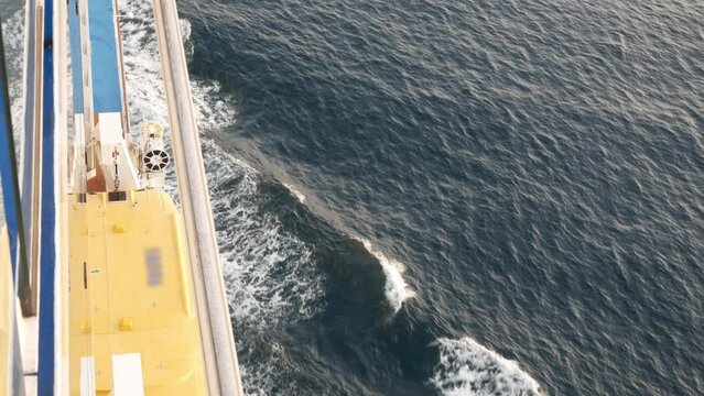 Lifeboat on giant cruise ship view down to ocean surface with waves below while ship cruising saling in the sea. safety muster lifeboat equipment.
