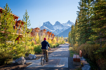People riding a bicycle on trail in residential area. Town of Canmore street view in fall season. Alberta, Canada. - obrazy, fototapety, plakaty