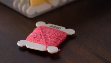Pink embroidery floss bobbin on a wooden background.