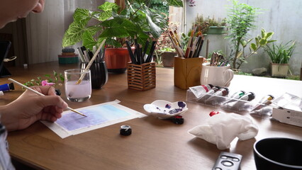 Painting with watercolor paints on wooden table in modern home office