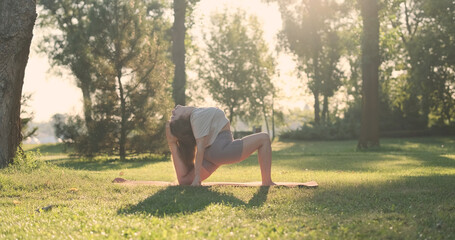 Yoga, woman gets into yoga pranayama pose, kneeling, throw head back. Side view, city park, lawn,...