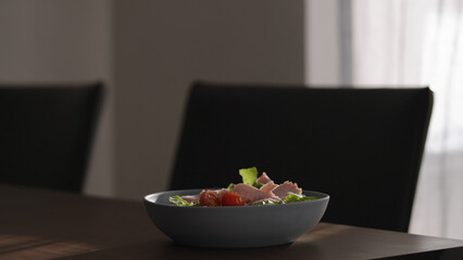 salad with tomatoes, lettuce and prosciutto cotto in blue bowl on wood table