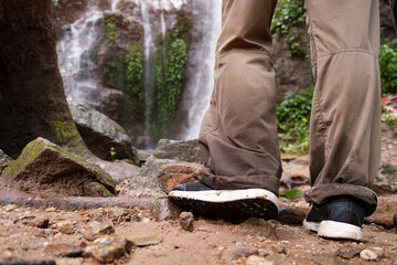 Legs of  female traveller standing in front of waterfall in tropical forest.