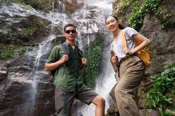 Young beautiful couple standing in front of a beautiful waterfall and posing for the camera.