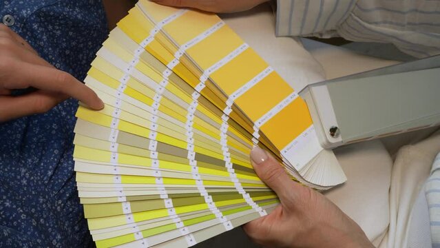 Female desiner and customer holding paint color swatches. Female hand holding color palette guide catalog with colour swatches. Designer's hand choosing color from various color swatches
