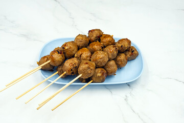 The delicious grilled beef meatballs and seasonings with a spicy sauce on dish with marble background. Grilled meatballs Made from meat. Asian Street Food. Roasted meatballs with sauce on blue plate.