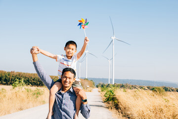 Father holds daughter with pinwheel enjoying. Family bonding near windmills signifies global...