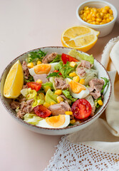 Fresh salad of tuna, egg, lettuce, cherry tomatoes, corn and lemon on a light background. Healthy nutrition concept, full bowl of salad.