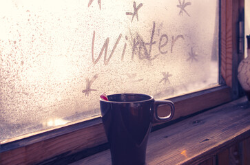hot warming drink in a mug in hands in woolen gloves against the background of the inscription...