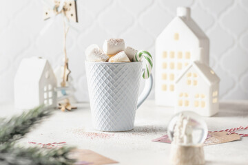 Hot cocoa or chocolate with marshmallow in blue ceramic mug surrounded by winter things on white table. The concept of cozy holidays and New Year.