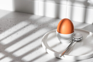 Boiled egg in hard light with window shadows on white kitchen background. Light protein breakfast concept, minimalism, high key - obrazy, fototapety, plakaty