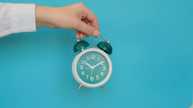 Hand holding a classic alarm clock on a blue background. 4k footage