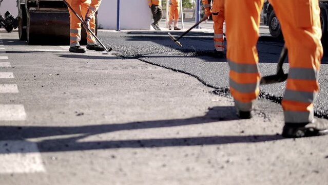 Steam rises from the hot asphalt surface. A worker levels fresh asphalt at a construction site.