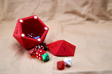 Several dice of different sizes and colors, with a red dice cup in the shape of a die on a...