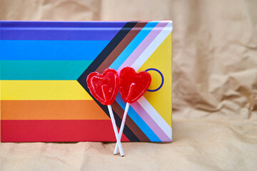 Two red heart-shaped lollipops with a background of the lgbtiq+ flag, representing love.