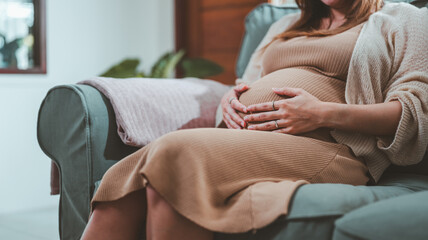 mother, woman, family, pregnant, pregnancy, baby, together, parenthood, maternity, motherhood. image of a pregnant woman embrace, her belly with two hands and her sit on sofa wait for maternity day. - obrazy, fototapety, plakaty