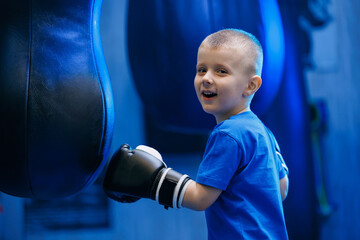 Portrait boy in black boxing gloves is training hit with punching bag. Sport photo kid boxer in gym
