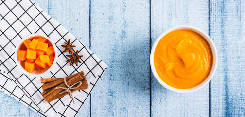 Organic pumpkin puree in a bowl, pumpkin and spices for cooking top view web banner
