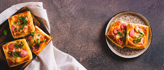 Square mini pie baked with tomato, sausage and cheese on a plate for a snack top view web banner - obrazy, fototapety, plakaty