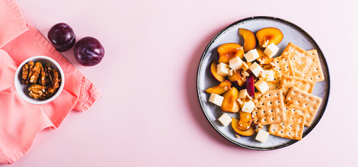 Dinner for girls, biscuits, cheese, plums and walnuts on a plate on pink top view web banner