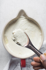 Scooping out homemade greek yogurt in a ceramic bowl with a spoon, process of making Greek yogurt, strained thick yogurt in white mixing bowl