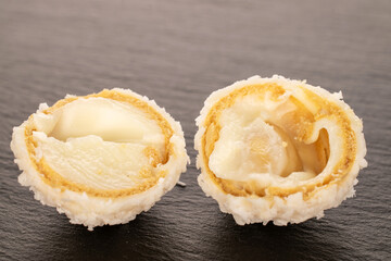 Two halves of candy with nut and coconut shavings on slate stone, macro.