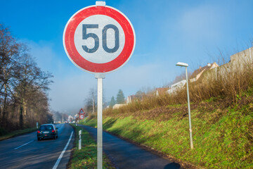 Verkehrsschild 50 km an Einfahrtsstrasse an Ortseingang mit Fahrradweg vor blauem Himmel